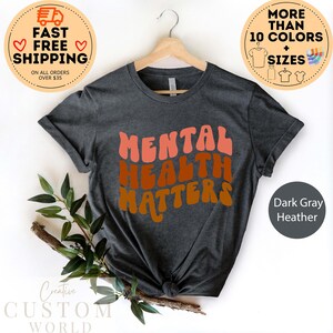May include: Dark gray heather t-shirt with the text "MENTAL HEALTH MATTERS" in a retro, colorful font.
