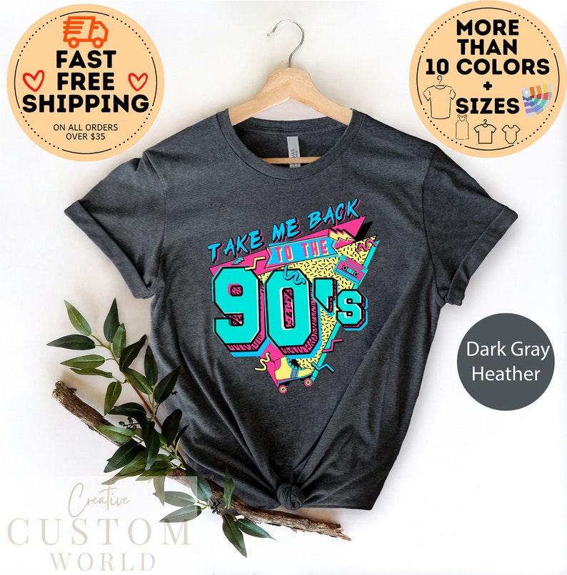 May include: Dark gray heather t-shirt with a retro design that says "Take Me Back to the 90's" in teal and pink. The graphic includes a boombox and roller skates. The shirt is displayed on a hanger.