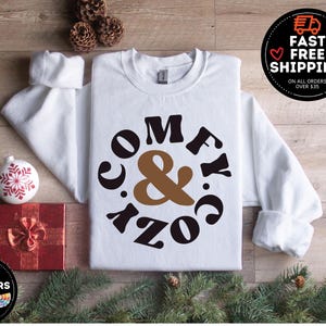 May include: White sweatshirt with a brown and black graphic that says "Comfy & Cozy" in a retro font.