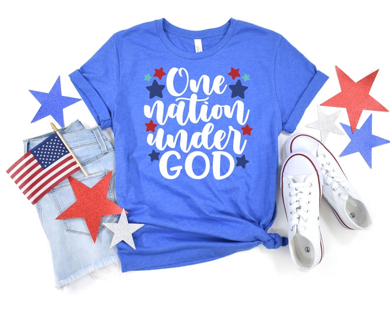 Op de afbeelding: Een blauw T-shirt met de tekst "One nation under GOD" in witte letters omringd door rode, witte en blauwe sterren.