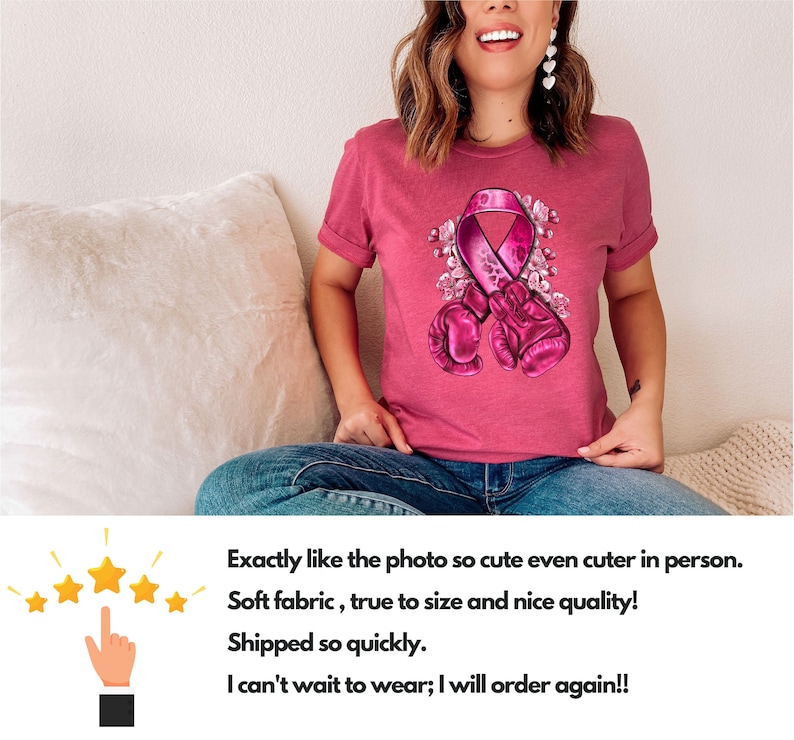 May include: Pink t-shirt with a pink ribbon and boxing gloves graphic. The ribbon is surrounded by flowers. The shirt is on a person sitting on a white couch.