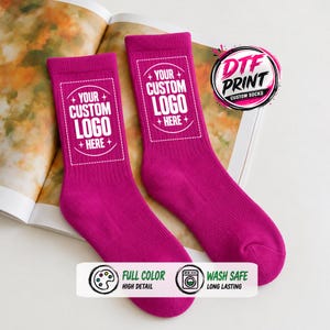 May include: A pair of vibrant magenta crew socks featuring a white rectangular graphic with the text YOUR CUSTOM LOGO HERE. The design includes small star accents. A circular logo in the corner reads DTF PRINT CUSTOM SOCKS, and a bottom banner highlights full color, high detail, wash safe, and long lasting features.