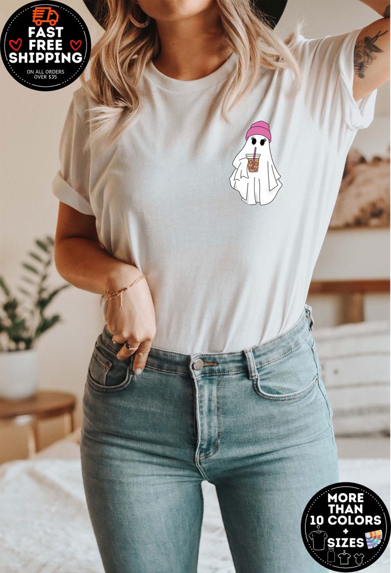 May include: White t-shirt with a graphic of a ghost wearing a pink beanie and holding a cup of iced coffee. The text "More than 10 Colors + Sizes" is visible in the lower right corner of the image.