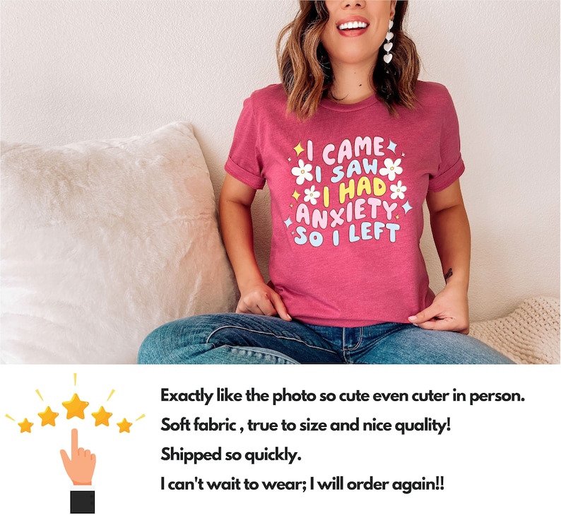 May include: A short-sleeved, magenta t-shirt with the text "I CAME I SAW I HAD ANXIETY SO I LEFT" in a colorful, playful font. The design includes flower and star graphics. The shirt is worn by a person.