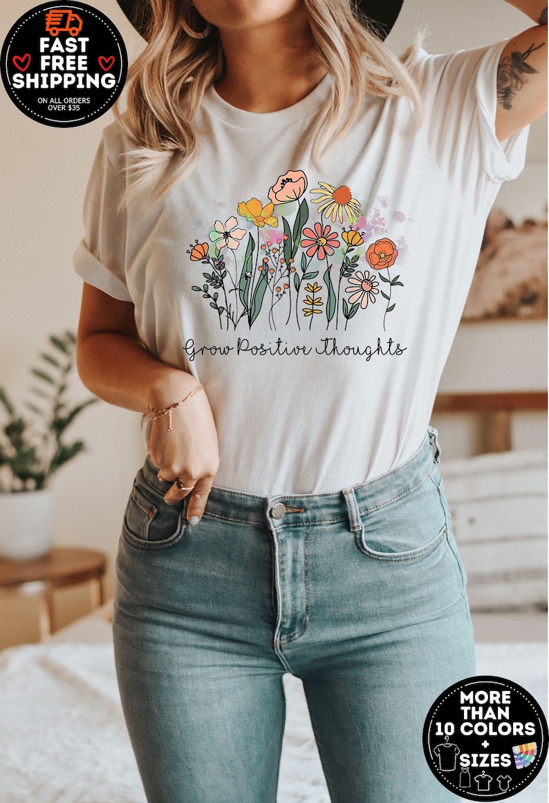 May include: White t-shirt featuring a colourful floral design and the text "Grow Positive Thoughts".