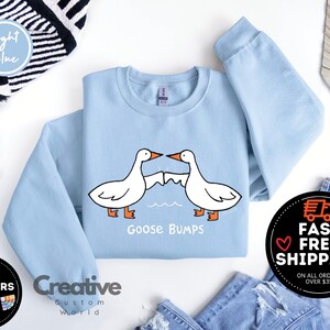 Puede incluir: Sudadera azul claro con un gr&aacute;fico de dos gansos que se miran con el texto "Goose Bumps".