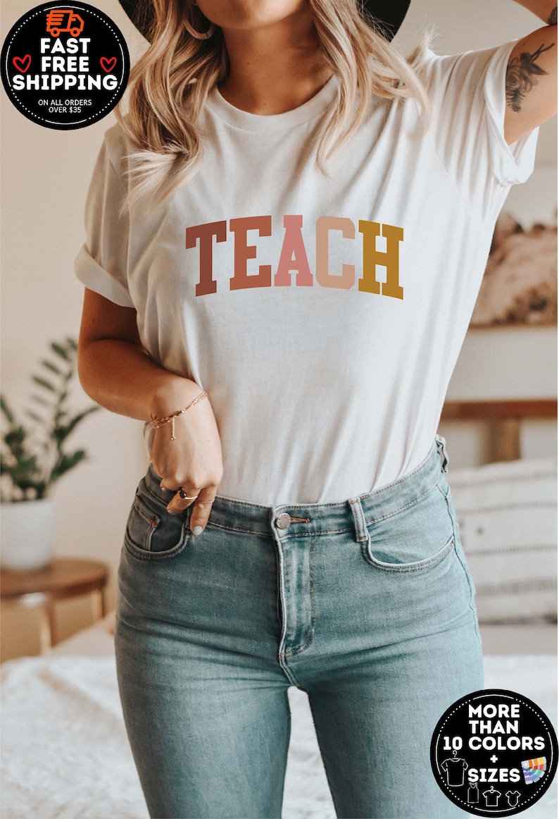 Może przedstawiać: Biały t-shirt z nadrukiem słowa "TEACH" w kolorowych literach. Litery są w odcieniach r&oacute;żowego, pomarańczowego i ż&oacute;łtego.