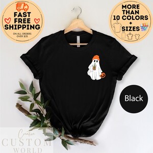 May include: Black t-shirt featuring a white ghost wearing an orange hat and holding a brown and orange cup. The ghost is holding a small orange pumpkin. The text "Black" is visible in the lower right corner of the image.