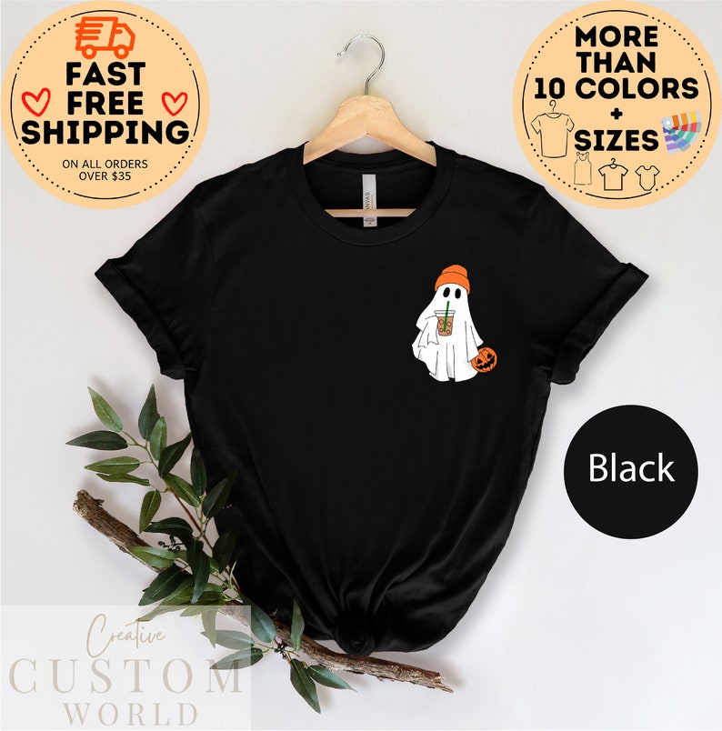 May include: Black t-shirt featuring a white ghost wearing an orange hat and holding a brown and orange cup. The ghost is holding a small orange pumpkin. The text "Black" is visible in the lower right corner of the image.