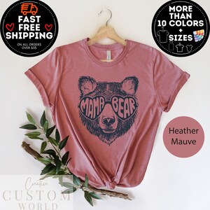 Puede incluir: Camiseta de color malva heather con un gr&aacute;fico de un oso con gafas de sol en forma de coraz&oacute;n que dicen "Mama Bear".