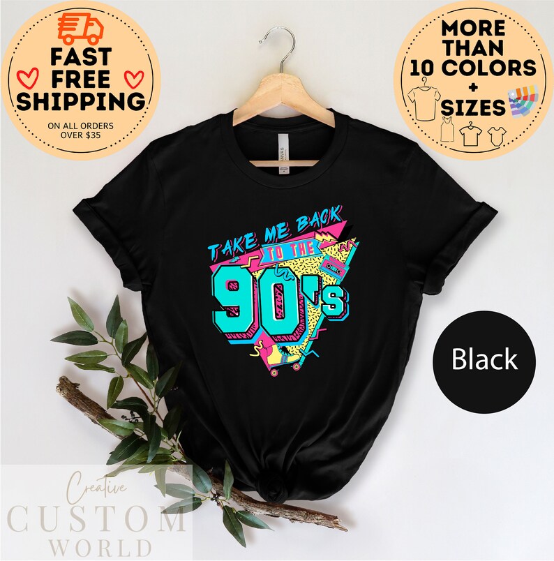 May include: Black t-shirt with a retro design that says "TAKE ME BACK TO THE 90's" in teal, pink, and yellow. The shirt is hanging on a wooden hanger. The shirt is available in more than 10 colors and sizes.