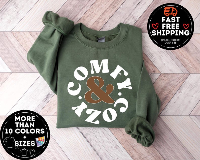 May include: A green sweatshirt with a white circle design that says "Comfy & Cozy" in a retro font. The ampersand is brown.