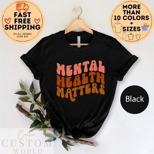 May include: Black t-shirt with the text "MENTAL HEALTH MATTERS" in a retro font with pink, orange, and brown colors.
