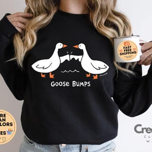 Puede incluir: Sudadera negra con un gr&aacute;fico de dos gansos que se miran con el texto "Goose Bumps".