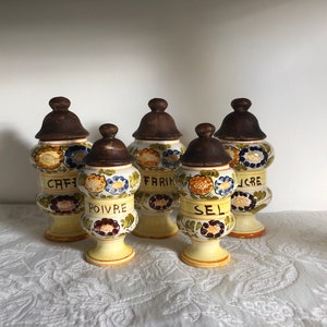 Puede incluir: Conjunto de cinco tarros de especias vintage de cerámica con diseños florales y tapas marrones. Los tarros están etiquetados con "CAFE", "POIVRE", "FARINE", "SEL" y "SUCRE".