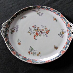 May include: A white ceramic serving platter with a blue, green and orange floral design. The platter has two handles and features a bird and butterfly motif.