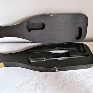 May include: A wooden box shaped like a wine bottle, with a lid that opens to reveal two thermometers and a hydrometer. The box is black with a gold trim.