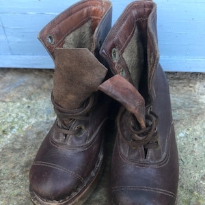 May include: A pair of brown leather boots with laces. The boots are worn and have a vintage look.