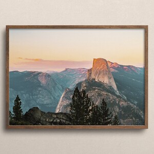 May include: A framed photograph of Half Dome, a granite cliff in Yosemite National Park, California. The image shows the iconic rock formation at sunset, with a soft pink and orange sky in the background.