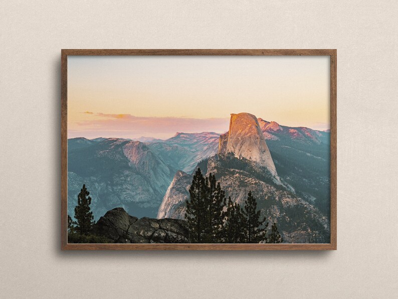 May include: A framed photograph of Half Dome, a granite cliff in Yosemite National Park, California. The image shows the iconic rock formation at sunset, with a soft pink and orange sky in the background.