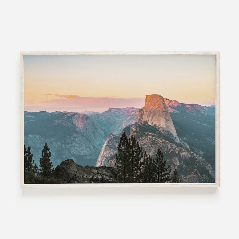 May include: A panoramic view of Half Dome, a granite rock formation in Yosemite National Park, California. The image captures the iconic peak at sunset, with soft pink and orange hues illuminating the sky and surrounding mountains.