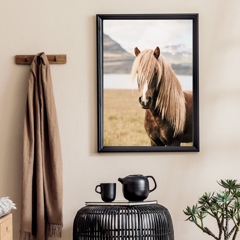 May include: A framed print of a brown horse with a long, light-colored mane. The horse is in a field with mountains and a lake in the background. A black teapot and cup sit on a black woven table.
