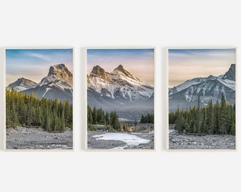May include: A three-part panoramic photograph of a mountain range with snow-capped peaks. The mountains are in the background, with a river in the foreground. The river is partially frozen, and there are trees on both sides of the river.
