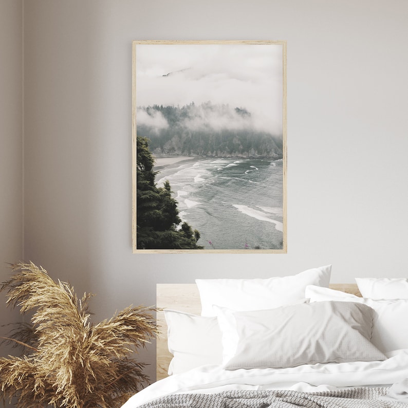 Puede incluir: Una fotograf&iacute;a de una costa brumosa con una playa y olas. La foto est&aacute; tomada desde un punto de vista elevado, mirando hacia abajo a la playa. Los &aacute;rboles en primer plano son verdes y el agua es azul.