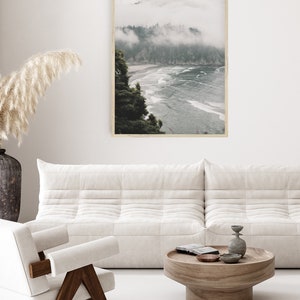 Puede incluir: Una fotograf&iacute;a enmarcada de una costa brumosa con una playa y olas. La foto est&aacute; colgada en una pared blanca sobre un sof&aacute; blanco y una mesa de caf&eacute; de madera.