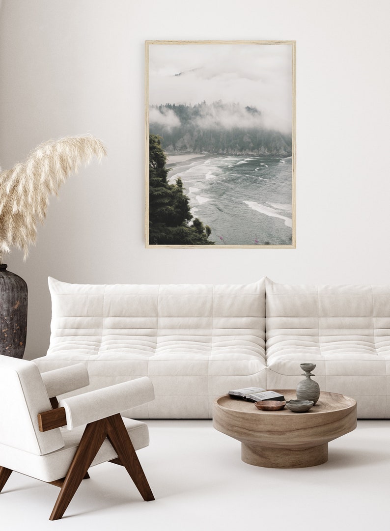 Puede incluir: Una fotograf&iacute;a enmarcada de una costa brumosa con una playa y olas. La foto est&aacute; colgada en una pared blanca sobre un sof&aacute; blanco y una mesa de caf&eacute; de madera.