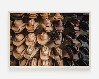 May include: A wall display of various cowboy hats in brown, tan, and black colors. The hats are arranged in rows and are hanging from hooks.