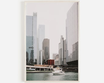 May include: A framed print depicting a cityscape with modern skyscrapers. A white boat is on the water in the foreground. The buildings are mainly glass and steel, with some brick structures. The sky is overcast.