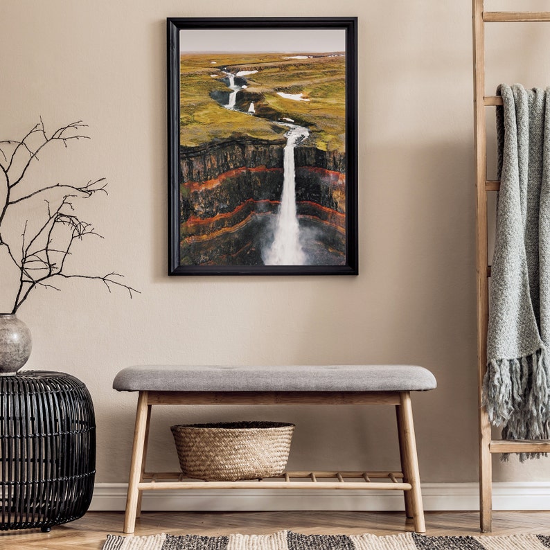 May include: A framed photograph of a waterfall cascading down a rocky cliff face. The waterfall is surrounded by green vegetation and the cliff face is layered with red, orange, and brown rock.