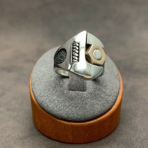 May include: A silver ring shaped like a wrench with a gold-colored nut on the end.