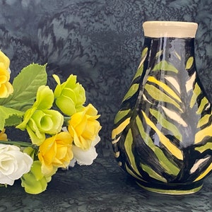 May include: A black ceramic vase with a green and yellow abstract pattern. The vase is sitting on a green and black textured surface.