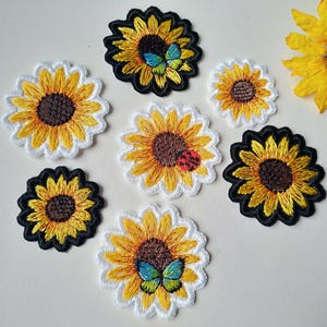 Könnte beinhalten: Ein Set mit sieben gestickten Bügelbildern mit Sonnenblumen, Schmetterlingen und Marienkäfern. Die Patches sind in verschiedenen Größen und Farben, darunter Gelb, Schwarz, Weiß und Rot.
