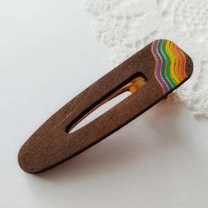 Puede incluir: Pinza de pelo de madera marrón oscuro con un diseño de arcoíris colorido en un extremo. La pinza mide aproximadamente 7,6 cm de largo y tiene un cierre metálico dorado.