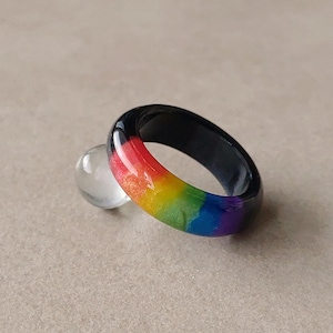 May include: A smooth, rounded ring featuring a vibrant rainbow gradient pattern on the outer surface, transitioning from red, orange, and yellow to green, blue, and violet, with a solid black interior band and a glossy, reflective finish.