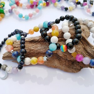 Peut inclure: Quatre bracelets en perles empilés sur un morceau de bois flotté. Les bracelets sont faits de perles noires, blanches, bleues, jaunes et orange. Un bracelet a un charme arc-en-ciel, un autre a un charme étoile et un autre a un charme croissant de lune.