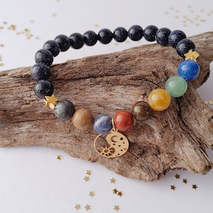 Può includere: Un braccialetto di pietre blu con un ciondolo dorato che presenta un design di sole e luna. Il braccialetto include anche sette pietre preziose di diversi colori.