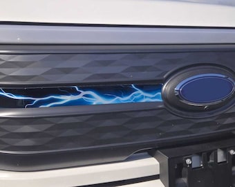 May include: Close-up of a white car's front grille with a black diamond pattern and a blue Ford logo. A blue lightning bolt graphic is centered on the grille.