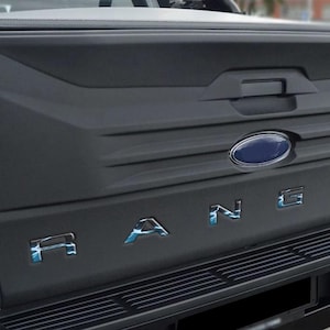 Könnte beinhalten: Die Rückseite eines weißen Ford Ranger Pickups mit einer schwarzen Heckklappe und einem blauen und silbernen "Ranger" Schriftzug. Das Ford Logo ist blau und silber.