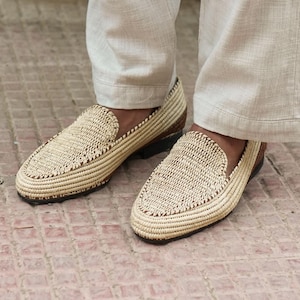 Puede incluir: Un par de mocasines de paja trenzada con ribete de cuero marr&oacute;n. Los mocasines se llevan con pantalones de lino beige claro.