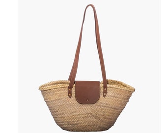 May include: A large, woven straw tote bag with brown leather handles and a brown leather flap. The bag has a curved shape and is perfect for carrying groceries or other items.