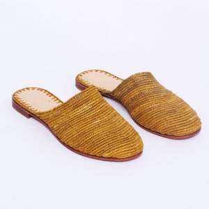 May include: A pair of woven straw yellow mules with a brown leather sole.