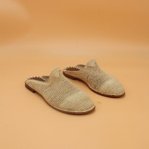 Könnte beinhalten: Ein Paar beige gewebte Slipper. Die Schuhe haben eine runde Spitze und einen niedrigen Absatz. Das Obermaterial besteht aus einem gewebten Material und die Sohle ist dunkelbraun. Die Schuhe sind für den lässigen Gebrauch konzipiert.