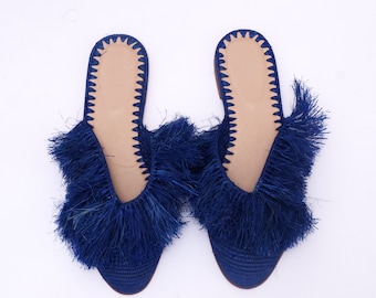 Op de afbeelding: Een paar blauwe geweven slippers met franjes. De slippers hebben een spitse neus en een platte zool.