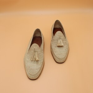 May include: A pair of beige woven leather loafers with tassel accents. The loafers have a pointed toe and a flat sole.