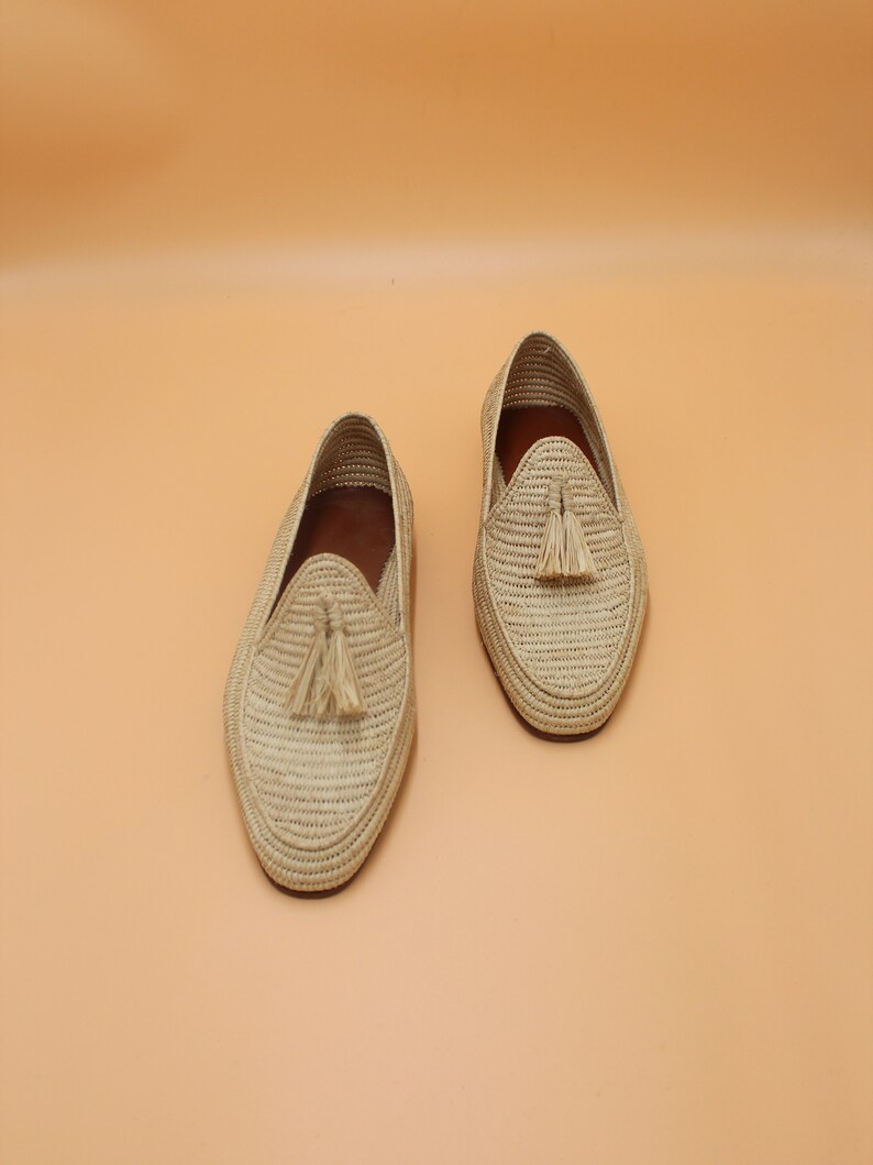 May include: A pair of beige woven leather loafers with tassel accents. The loafers have a pointed toe and a flat sole.