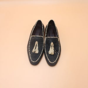 K&ouml;nnte beinhalten: Ein Paar schwarze geflochtene Lederschuhe mit Quaste. Die Schuhe haben eine wei&szlig;e Naht an den R&auml;ndern.